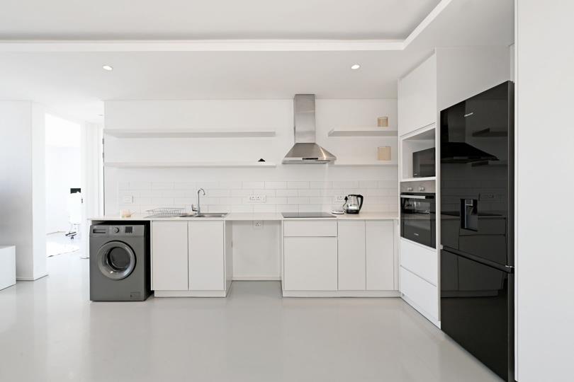 White galley kitchen with handleless flat-panel cabinetry, subway-tile splashback, stainless-steel canopy extractor, built-in oven and microwave tower, black French-door refrigerator, and a freestanding washing machine b