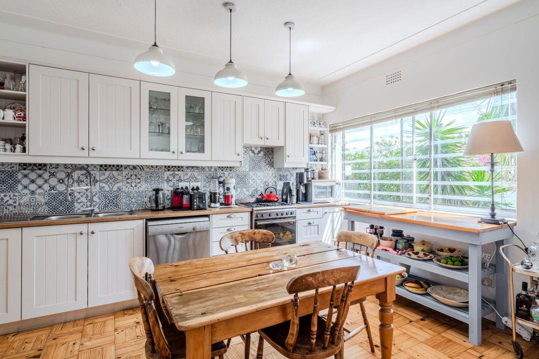 Renovated kitchen with white shaker-style cabinetry, blue-and-white decorative tile splashback, solid wood countertops, stainless steel dishwasher, gas/electric range, pendant lights, and a large window overlooking the g