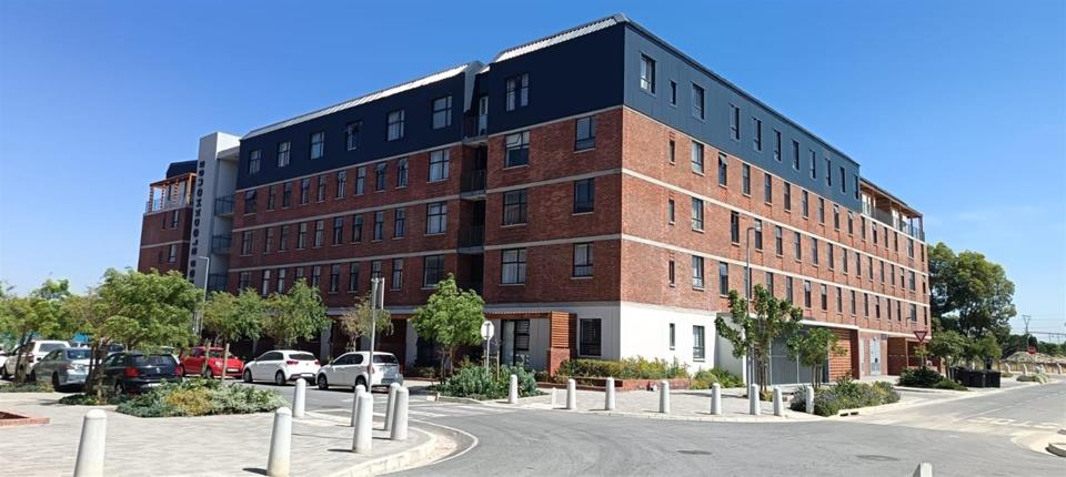 Wide-angle corner view of Kings Blockhouse revealing the complete building footprint with red-brick facade, blue-grey pitched roof, white ground-floor base, a landscaped roundabout with bollards, and vehicles parked on t