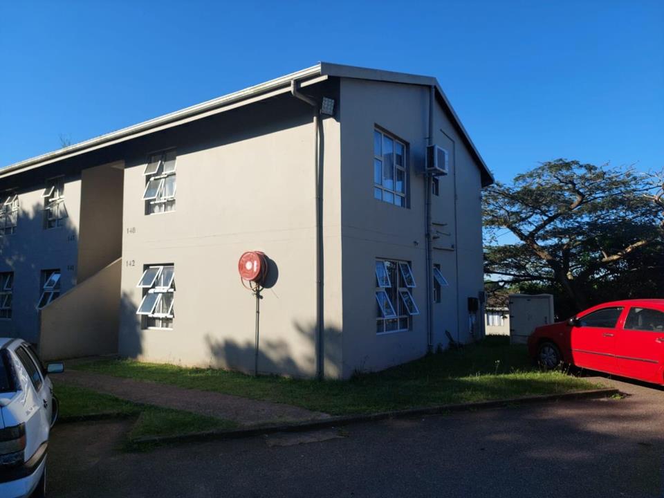 Exterior view of a two-storey grey-rendered apartment block (units numbered 142, 148 visible) in Northridge Park, Montclair, with unit numbers on the facade, white aluminium casement windows, a red fire hose reel on the 
