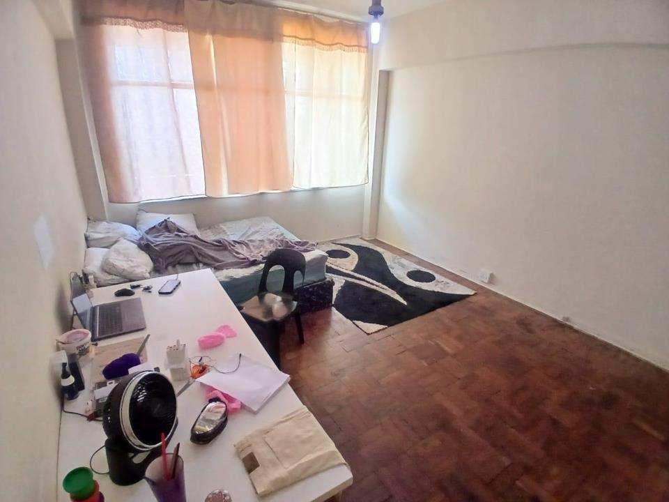 Second bedroom or same bedroom from opposite angle showing parquet flooring, a mattress on the floor with bedding, a white desk with a laptop and personal items, a patterned area rug, sheer curtains on a large window, an
