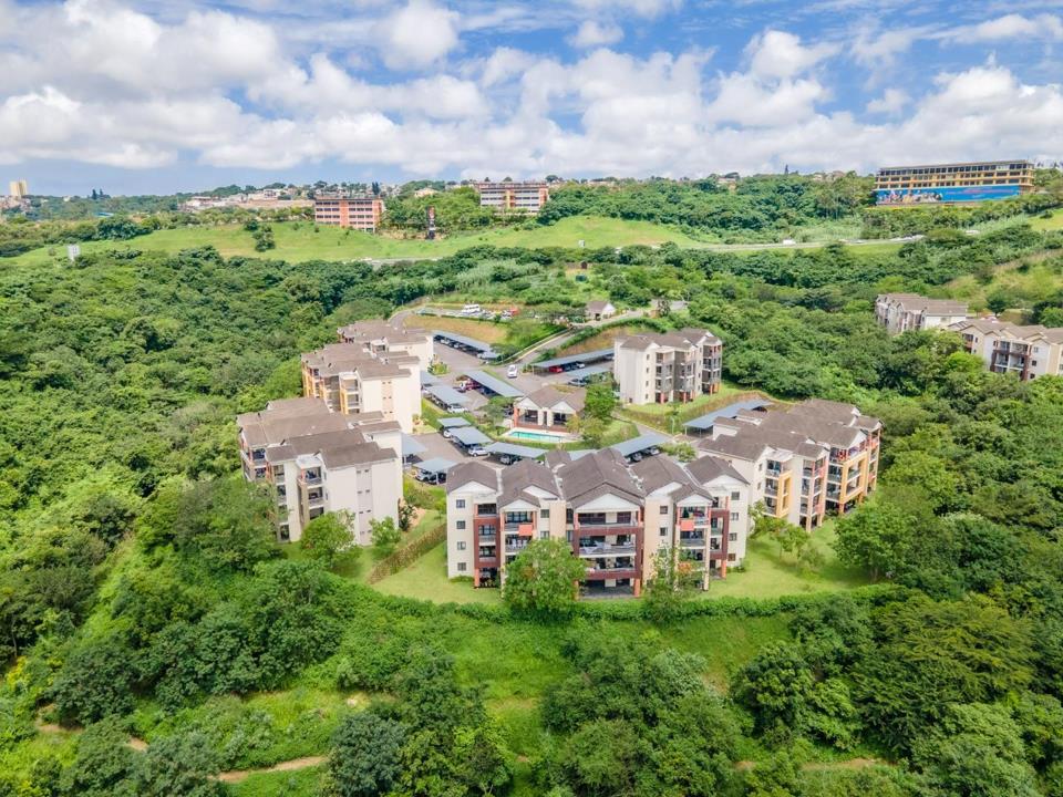 Wide-angle aerial drone view of Westwood Terraces complex set among dense indigenous bush in Westville, showing multiple four-storey residential blocks arranged around a central courtyard with a visible pool.