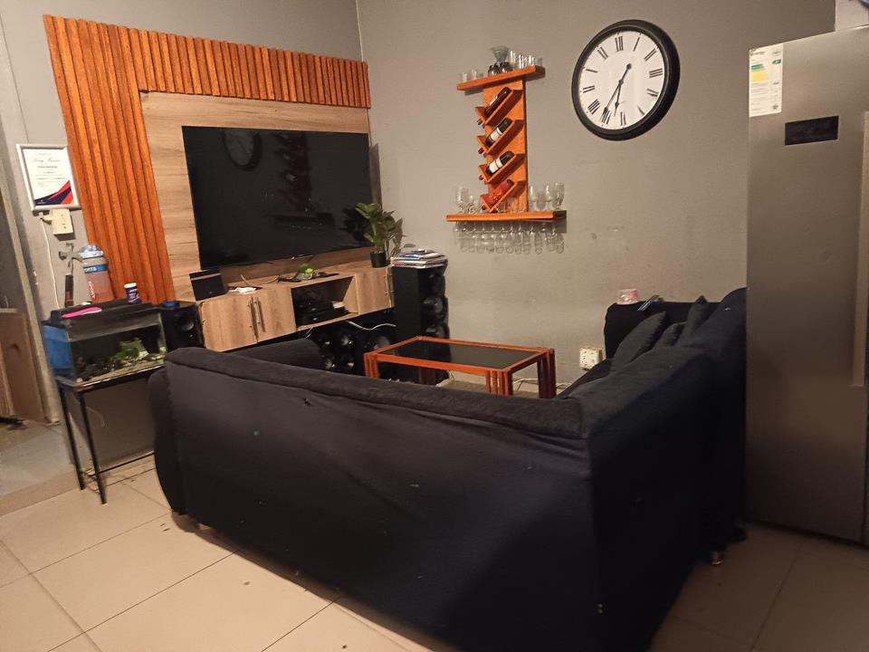 Open-plan living room viewed from behind a large dark navy sofa, showing a timber-slat feature wall with a wall-mounted flat-screen TV, a timber TV unit with lower cabinetry, a wall-mounted wine rack with bottles and ste