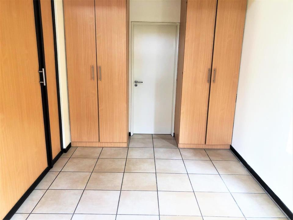 Bedroom with full-height built-in oak-finish wardrobes spanning both side walls, tiled floor, and a central white interior door leading to what appears to be the en-suite bathroom.