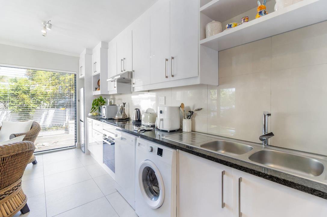 Well-fitted galley kitchen with white high-gloss upper and lower cabinets, dark granite-effect countertops, tiled splashback, stainless steel double sink, under-counter oven, dishwasher, front-loading washing machine, an