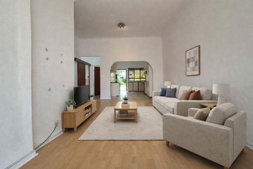 Staged lounge viewed from the rear wall, revealing the arched opening leading through to the kitchen and garden beyond, high plastered ceilings, wood floors, and the TV area against the left wall.