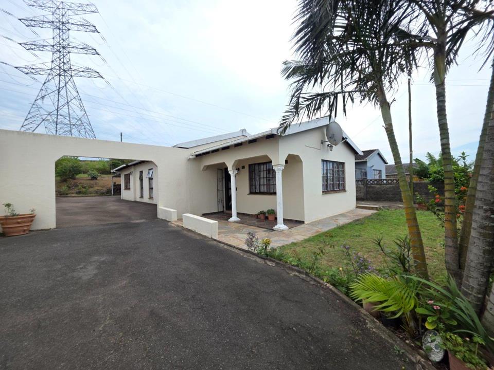 Front exterior of a single-storey plastered house in Newlands West showing a covered entrance porch with white columns, burglar-barred windows, a paved driveway, manicured front garden with palm tree, and a large power t