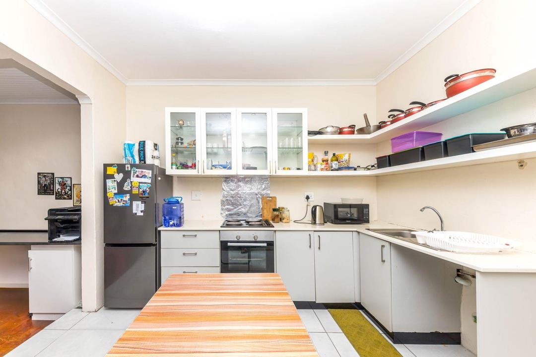 Spacious kitchen viewed from the dining end, showing full run of grey-and-white base and wall cabinets, open shelving with cookware, fridge-freezer, Bosch oven and hob, double sink, striped runner rug on white ceramic ti