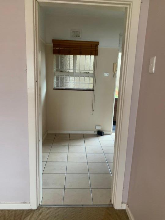 View through a doorway into a tiled passage or small room with a frosted-glass security window fitted with a bamboo roller blind, light-painted walls, and a wall socket visible.