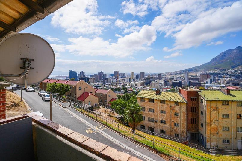 Balcony view from the apartment showing a satellite dish in the foreground, the Cape Town CBD skyline with harbour cranes visible in the mid-distance, and the slopes of Table Mountain to the right under a partly cloudy s
