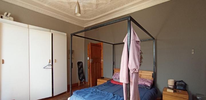 Bedroom featuring an industrial-frame steel four-poster bed surround, a double built-in wardrobe with white doors, a wooden bedside table, and a decorative plaster ceiling with a pendant light fitting.