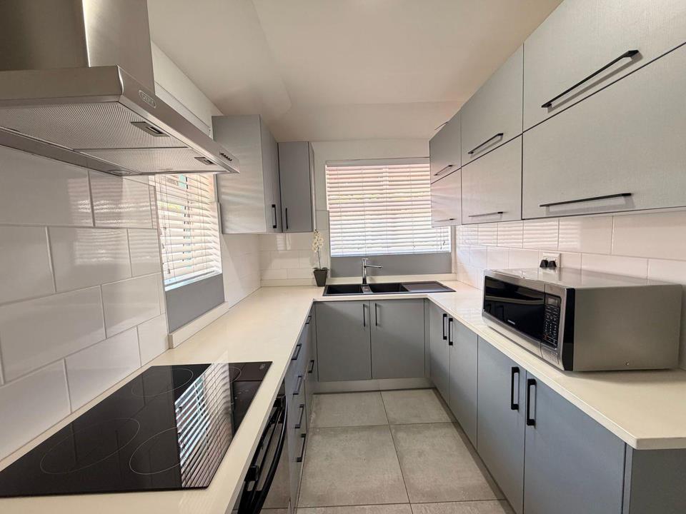 Newly renovated U-shaped kitchen with grey flat-panel cabinetry, white quartz-effect countertops, white subway-tile splashbacks, a black ceramic hob, stainless-steel canopy extractor, double under-mount sink, and a Samsu