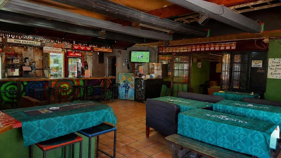 Listing number: P24-117680027, Image number: 2, The main bar and its seating: a painted counter with stools, fridges and a television behind it, and tables under green cloths